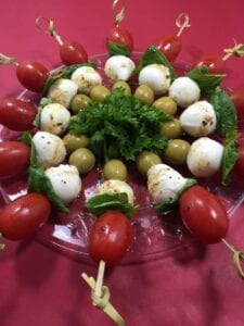 skewered tomatoes, basil, cheese and green olives on clear plate