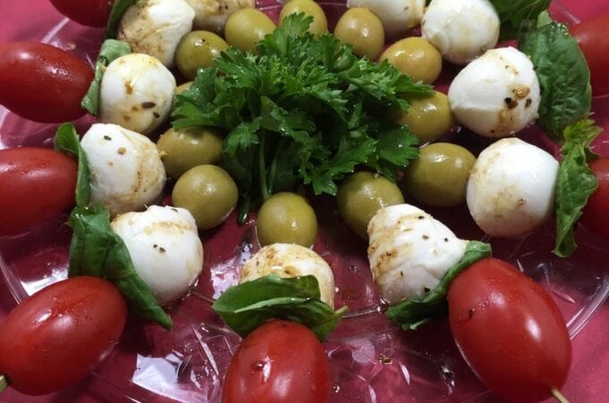 skewered tomatoes, basil, cheese and green olives on clear plate
