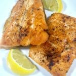 Baked Char salmon on a white plate with lemon slices