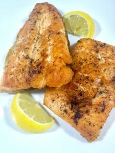 Baked Char salmon on a white plate with lemon slices