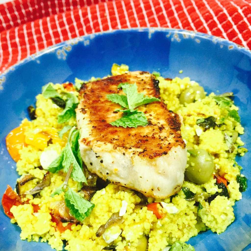 Curry Vegetable Couscous topped with a pork chop in a blue bowl.