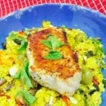 Baked pork chop resting on curry vegetable couscous on a blue plate.