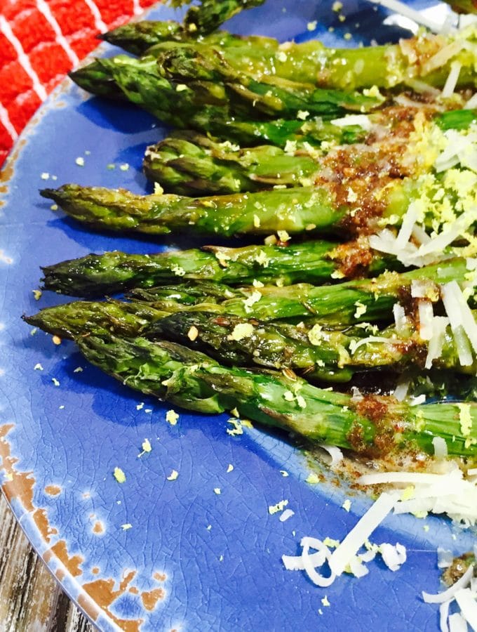 Cooked asparagus with browned butter on a blue plate