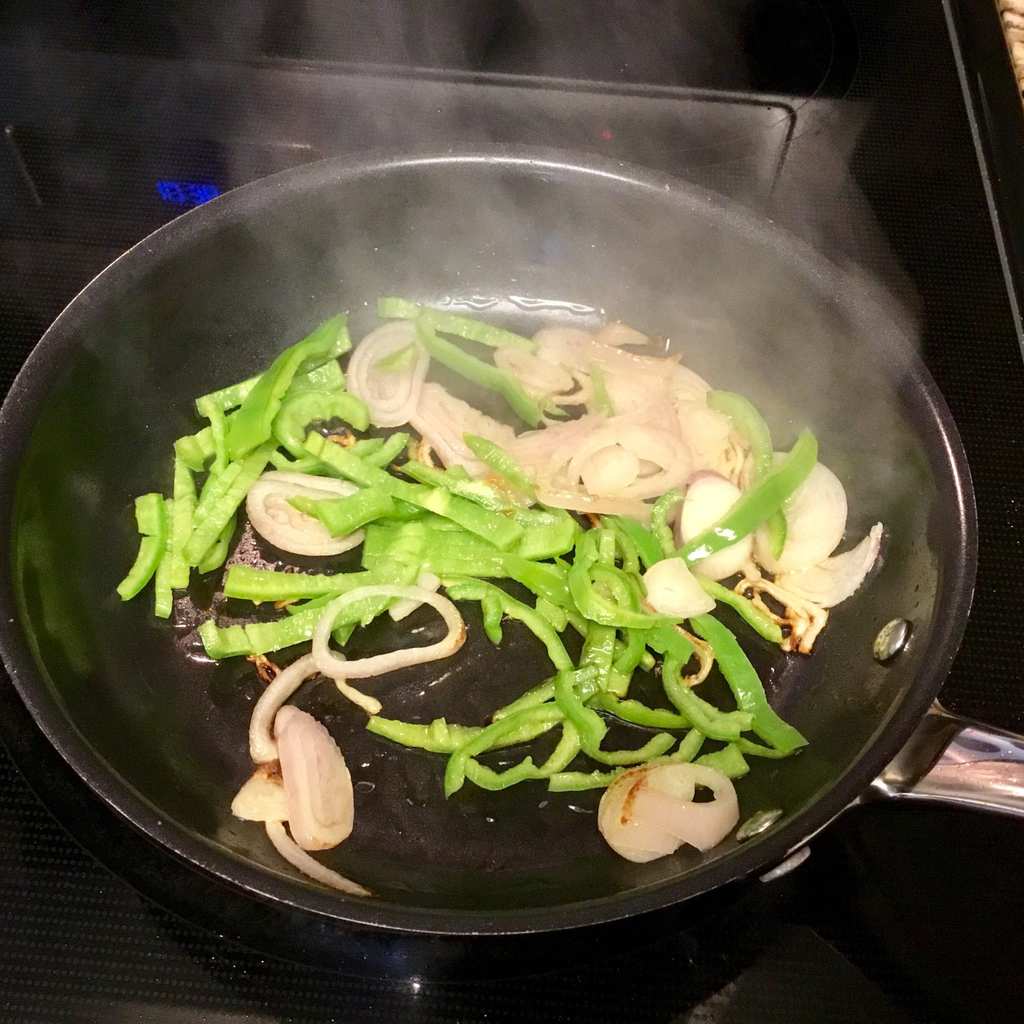 Onions and Anaheim peppers sautéing in a pan