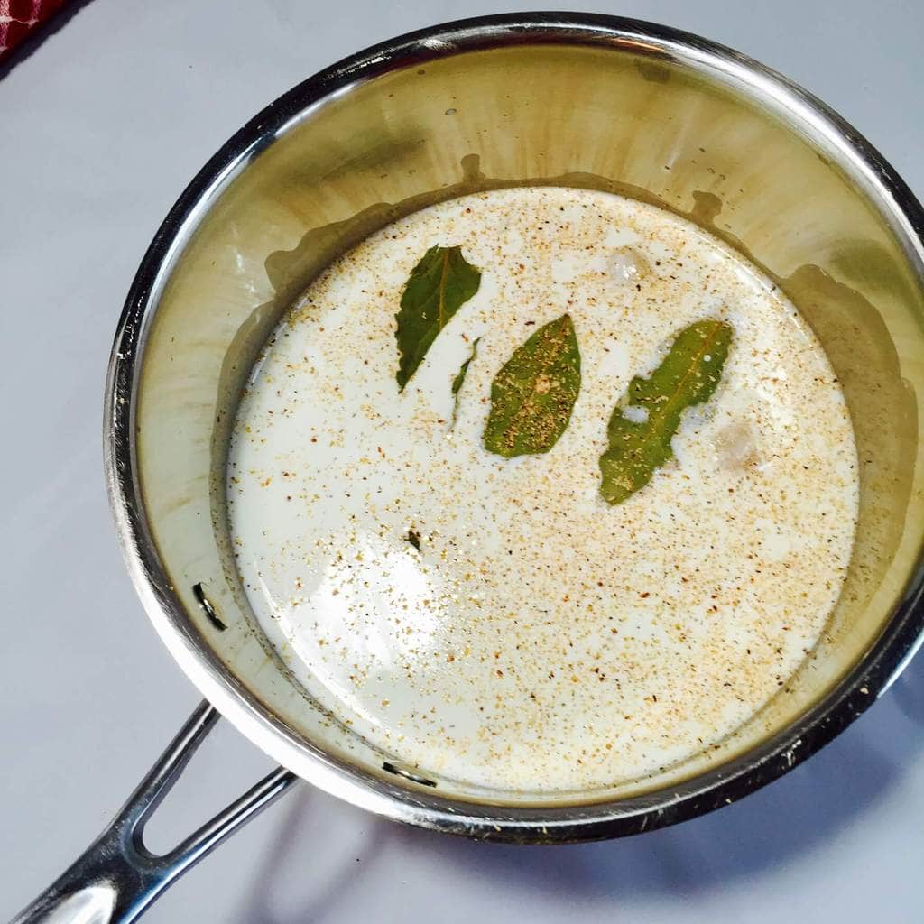 Cream in saucepan with bay leaves and spices