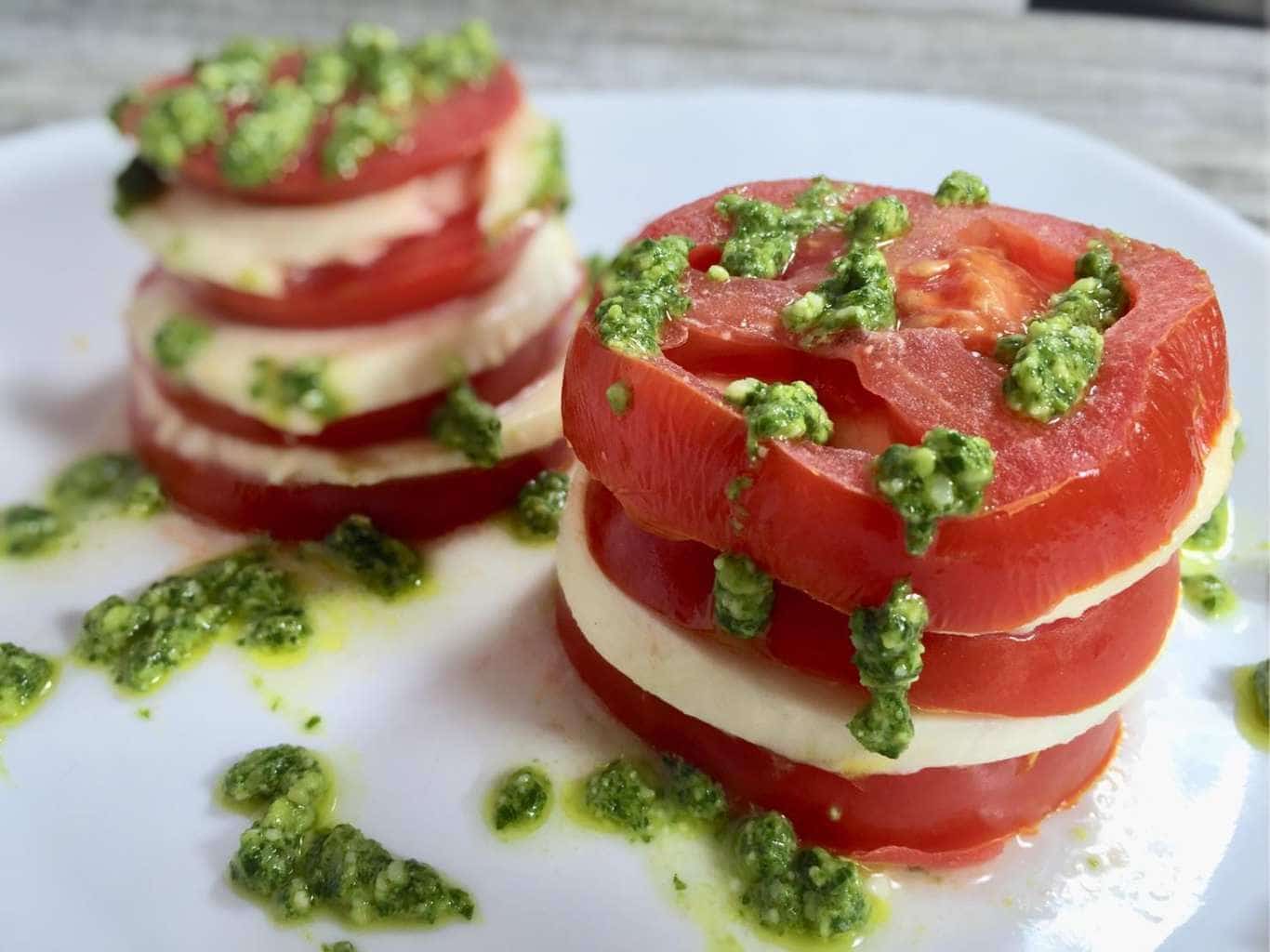 Stacked tomato salad with pesto on a white