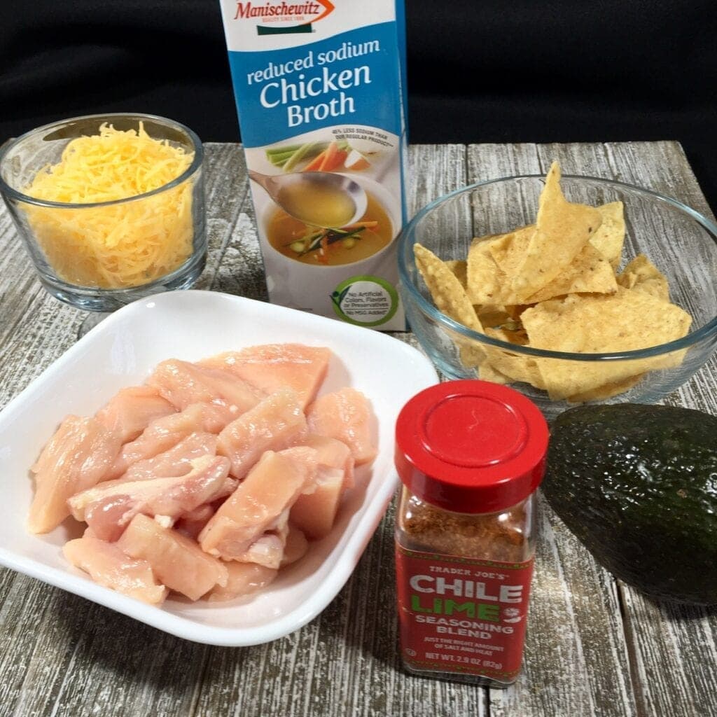 Raw chicken in white bowl, Chile Lime Seasoning, tortillas, grated cheese and chicken broth on a wooden table