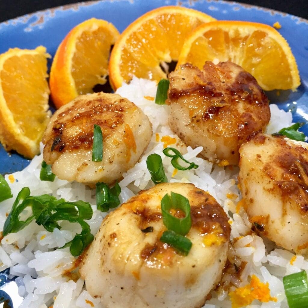 Sautéed sea scallops with sauce over rice with chive garnish