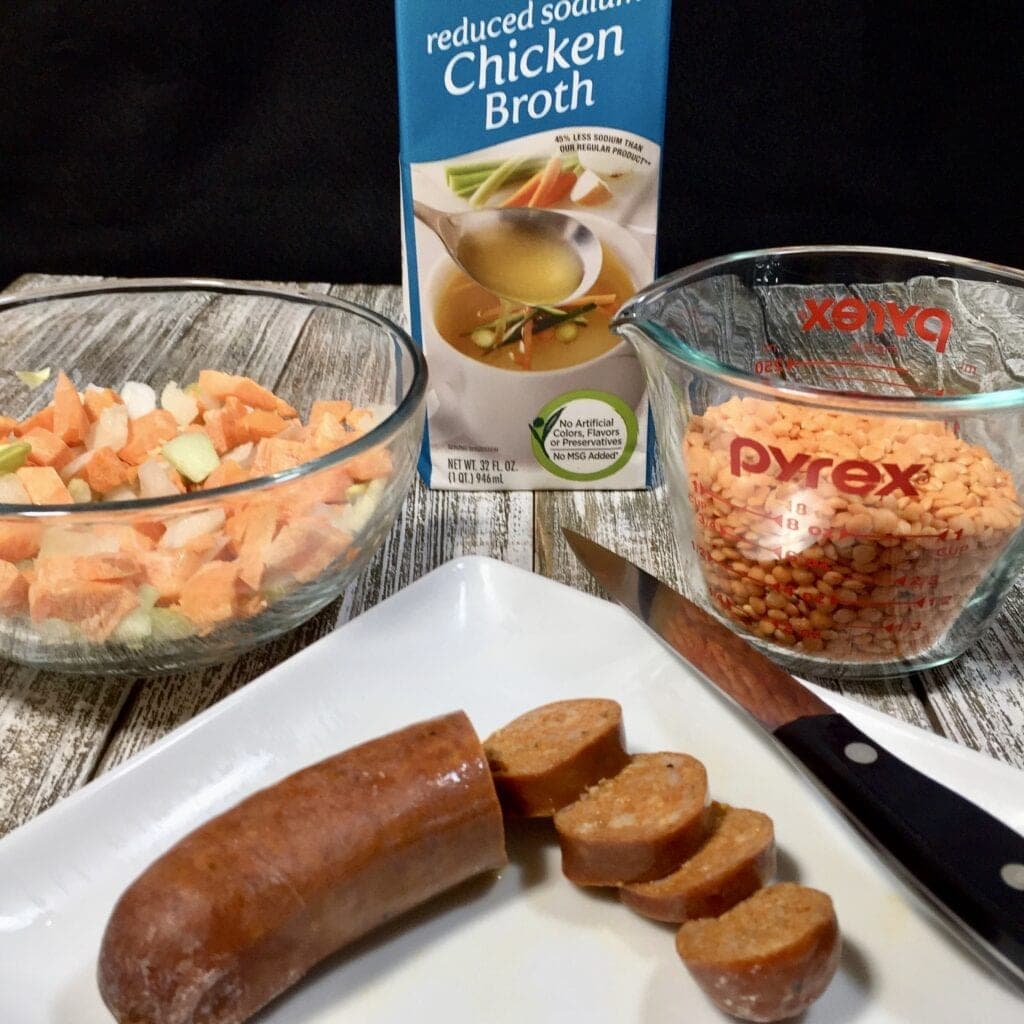 Chopped vegetables, red lentils and chopped sausage on a wooden table