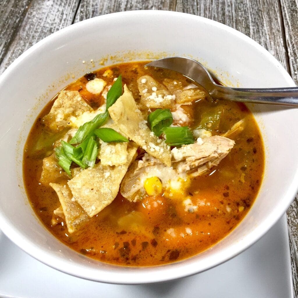 A white bowl of chicken soup with tortillas and Cotija cheese