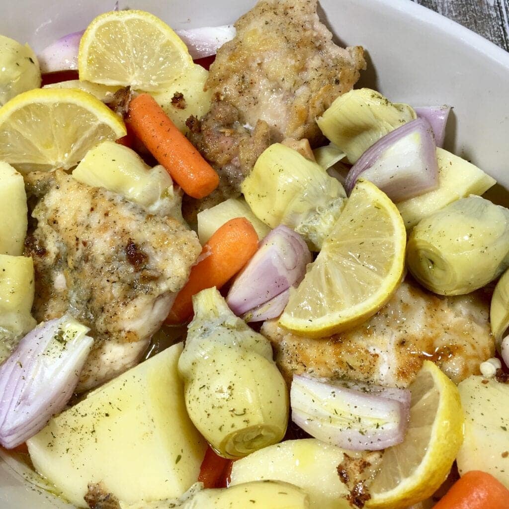 browned chicken, carrots, shallots, potatoes and lemons in a pan ready to bake