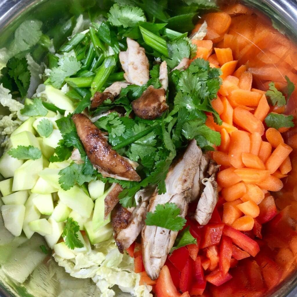 Carrots, chicken, cucumbers onions and cilantro in a metal bowl