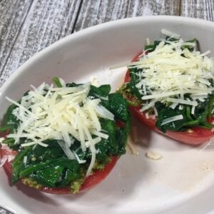 two tomato halves topped with cooked spinach and parmesan cheese in white bowl