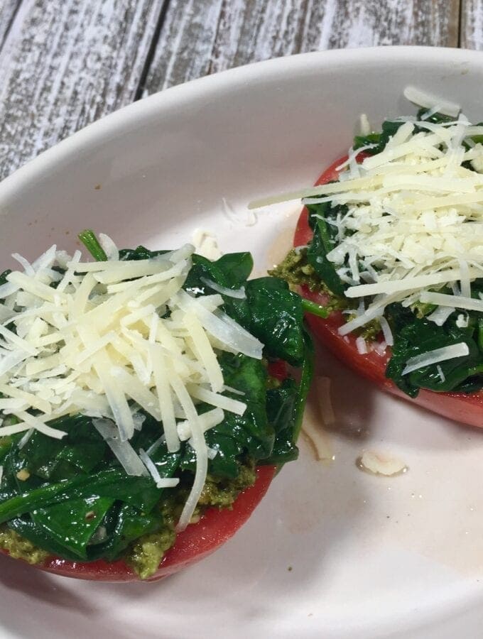 two tomato halves topped with cooked spinach and parmesan cheese in white bowl