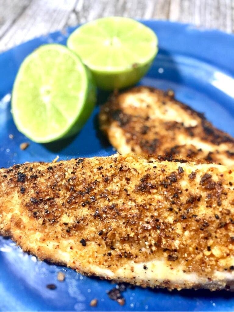 two cooked fillets of tilapia on a blue plate with limes