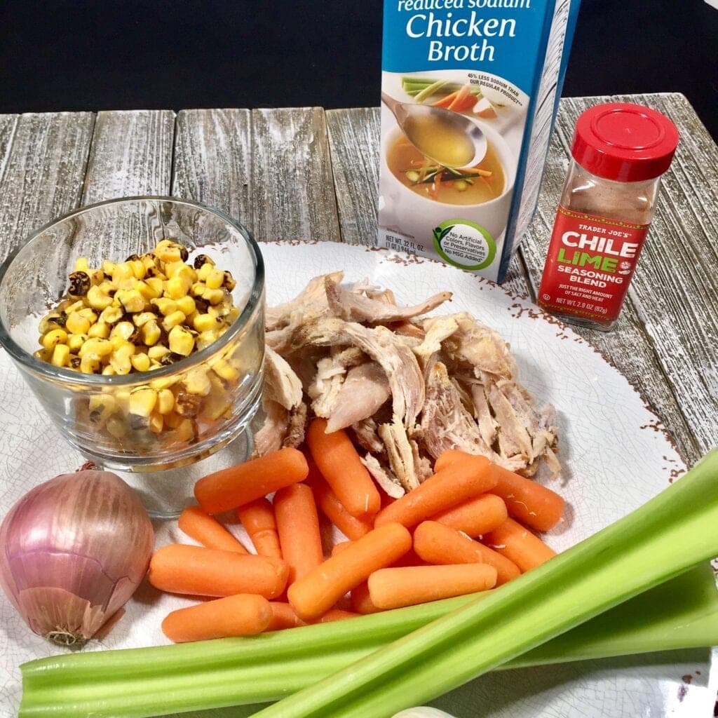 Corn, carrots, celery, onions and chicken on a white plate with chicken broth and Chile Lime Seasoning
