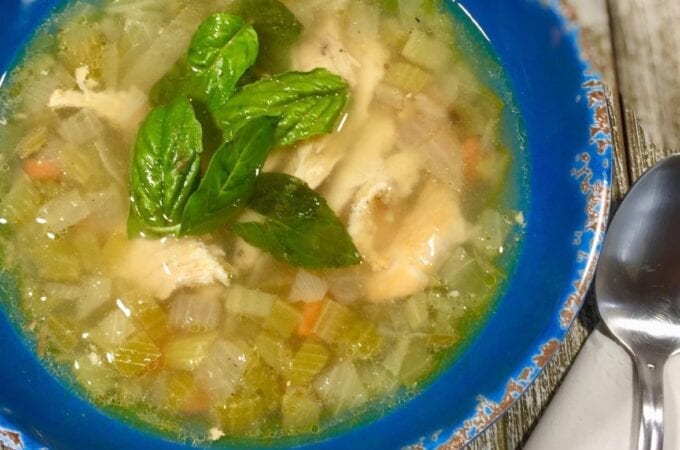 Chicken and vegetable soup in a blue bowl on a wooden table
