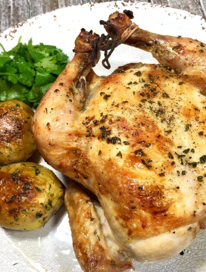 Crispy Roasted Chicken on a white plate with potatoes and parsley