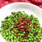 English peas topped with crispy prosciutto in a white bowl