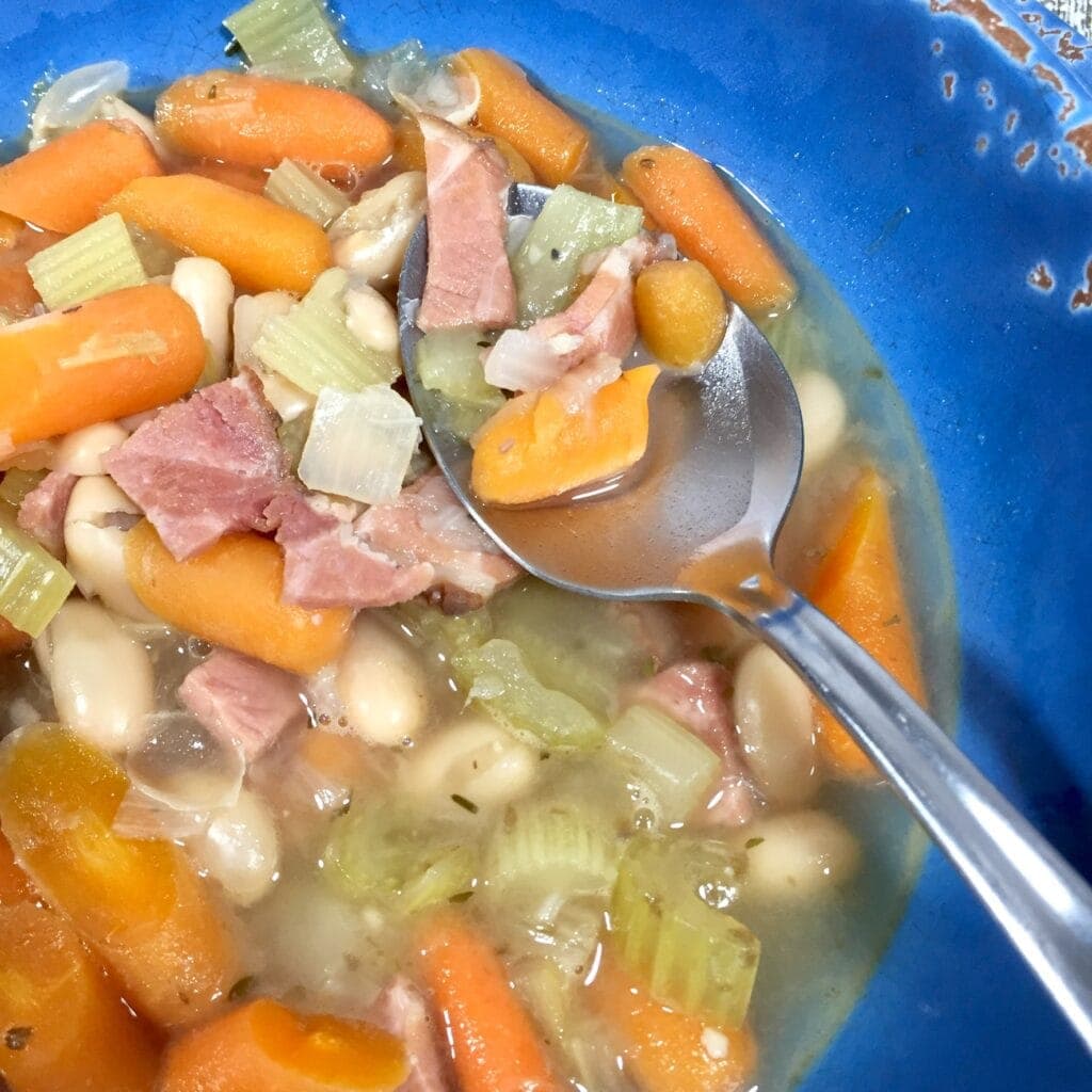 a bowl of Ham and Bean Soup pin a blue bowl with a spoon