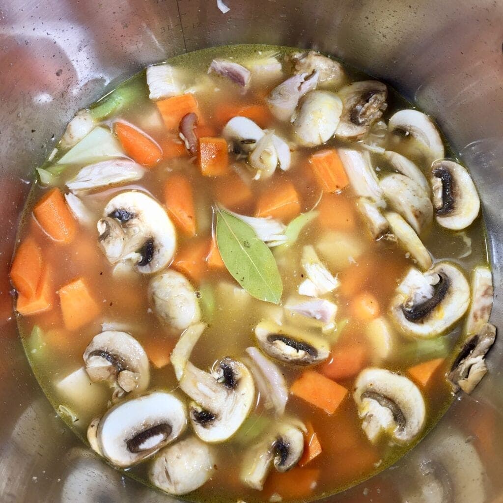 chicken soup in a pot simmering with a bay leaf