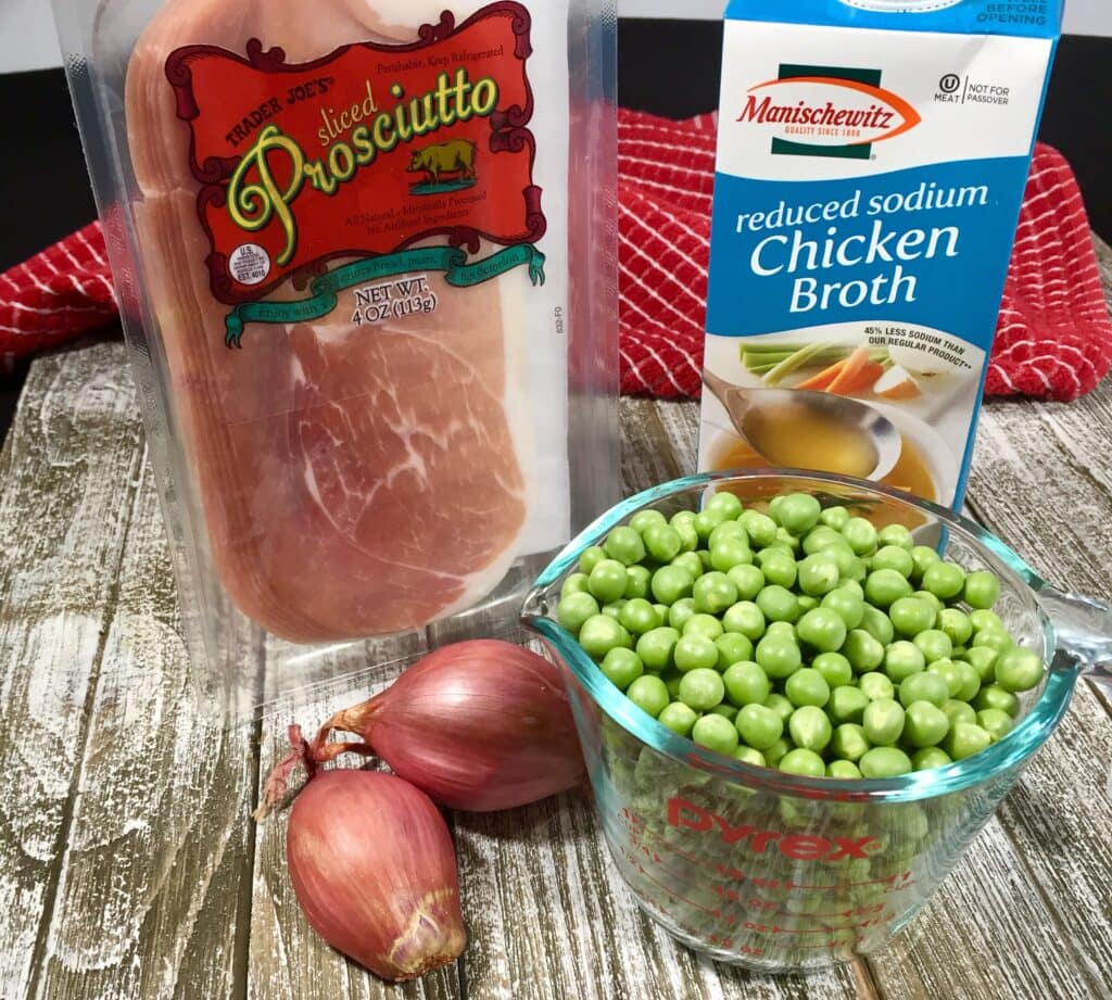 English peas, prosciutto, shallots and a container of chicken broth on a wooden table