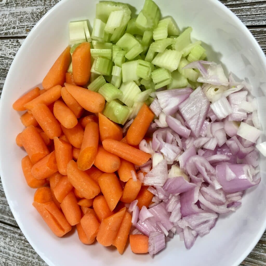 Diced celery, carrots and onion in a white bowl