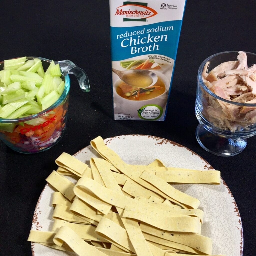 pappardelle noodles, vegetables, chicken and packaged chicken broth against a black background