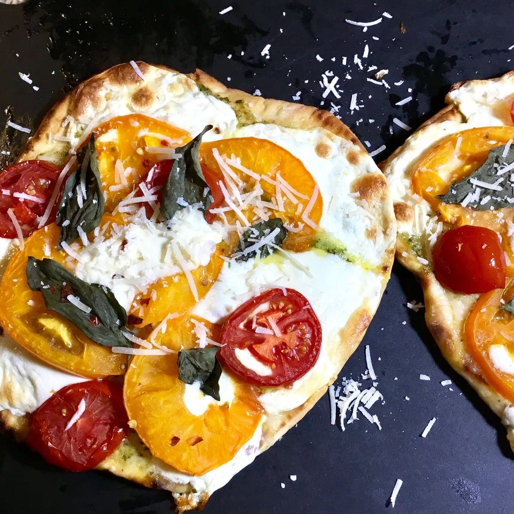 Baked naan pizza with tomatoes, cheese and basil on a black cutting board