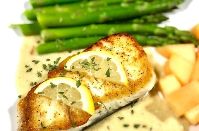 Baked halibut with lemon slices on a bed of tarragon cream sauce