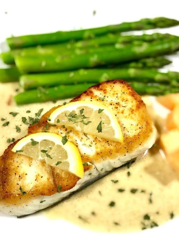 Baked halibut with lemon slices on a bed of tarragon cream sauce