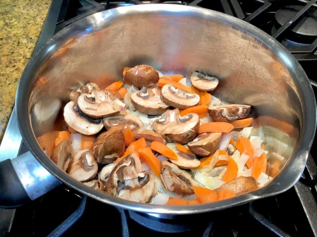 Mushrooms, onions and carrots cooking in a soup pot.