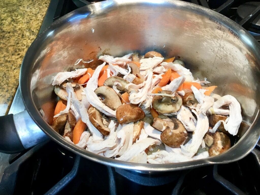 Mushrooms, shallots, carrots and chicken in a soup pot cooking on the stove