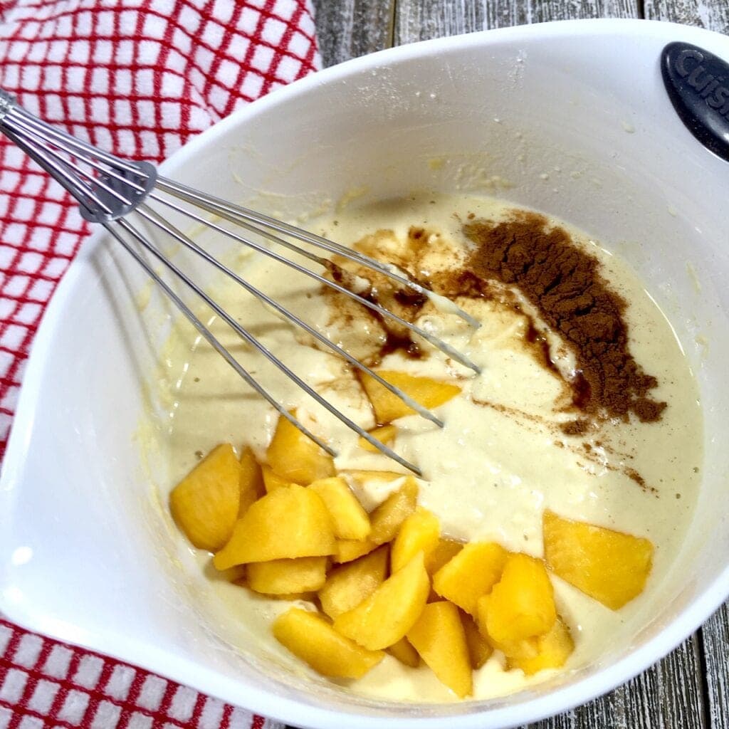 Pancake batter in a white bowl with cinnamon and diced peaches