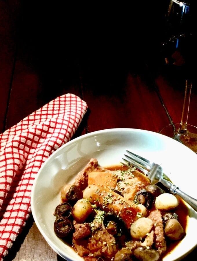 Julia's Easy Coq au Vin in a white dish with a red napkin and a glass of wine