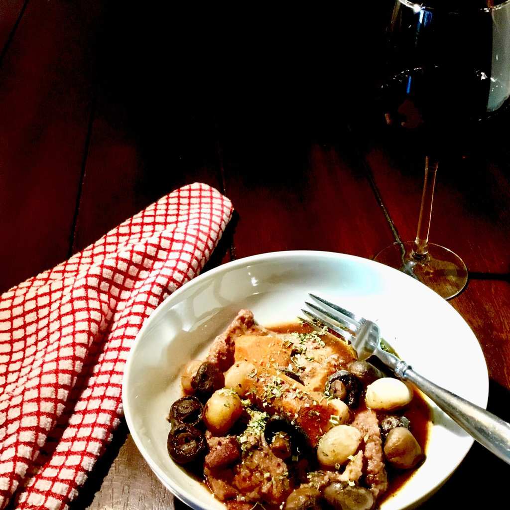 Julia's Easy Coq au Vin in a white dish with a red napkin and a glass of wine