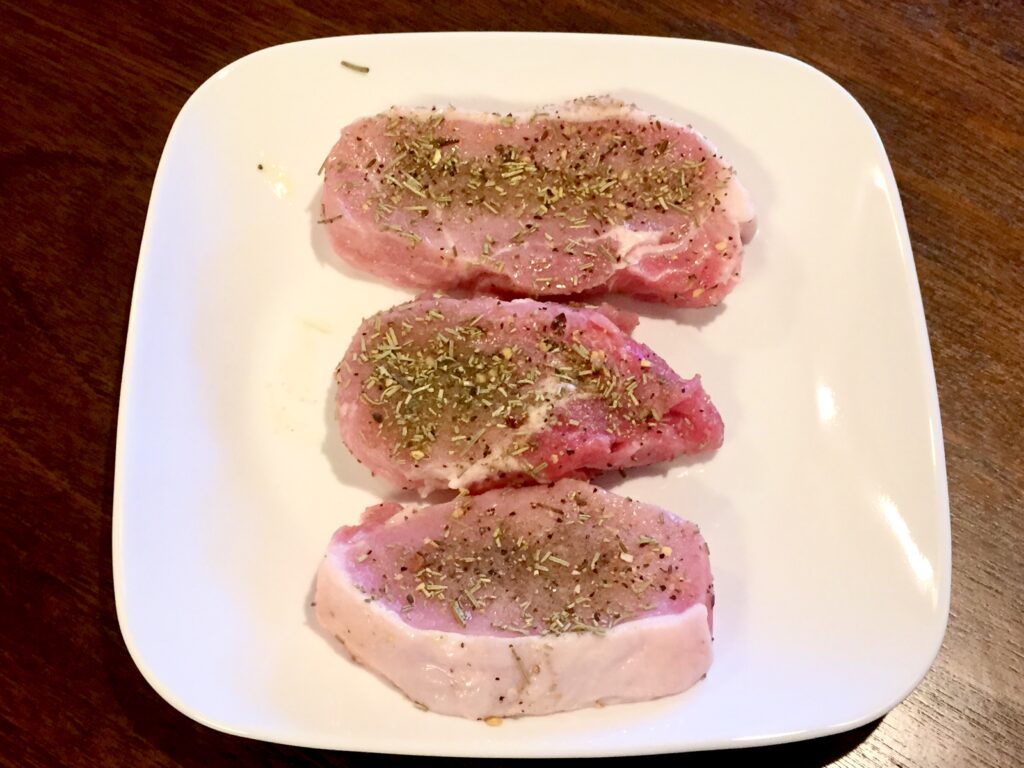 Savory Pork chops with a spice rub on a white plate ready to cook